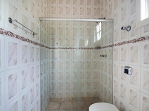 Un baño con ducha, paredes de azulejos y retrete.
