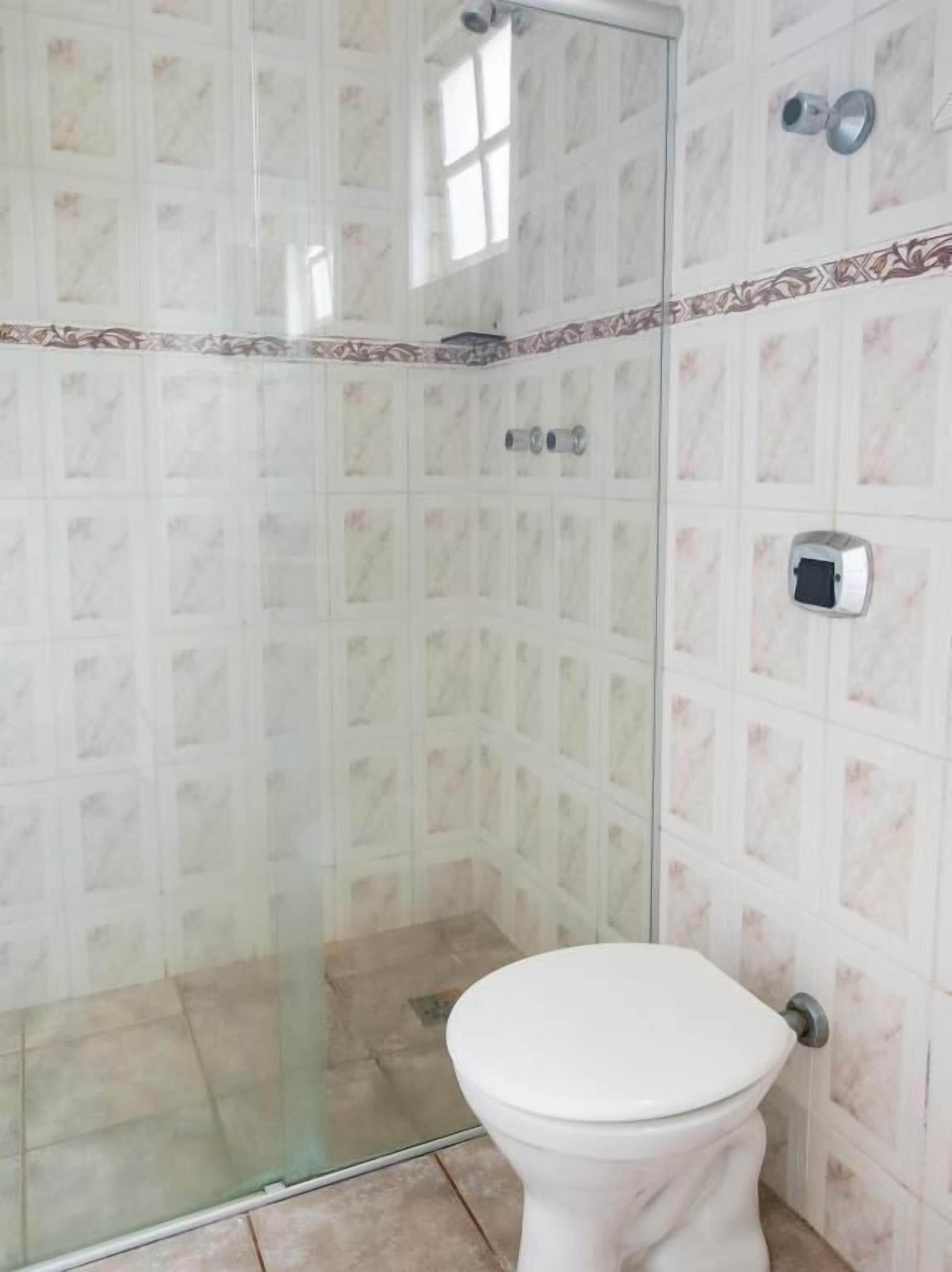 Casa de banho com cabine de duche em vidro, sanita e paredes revestidas a azulejos.