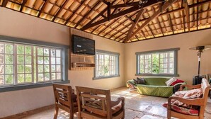 Ein geräumiger Raum mit hohen Decken, großen Fenstern, einem grünen Sofa und Holzstühlen.