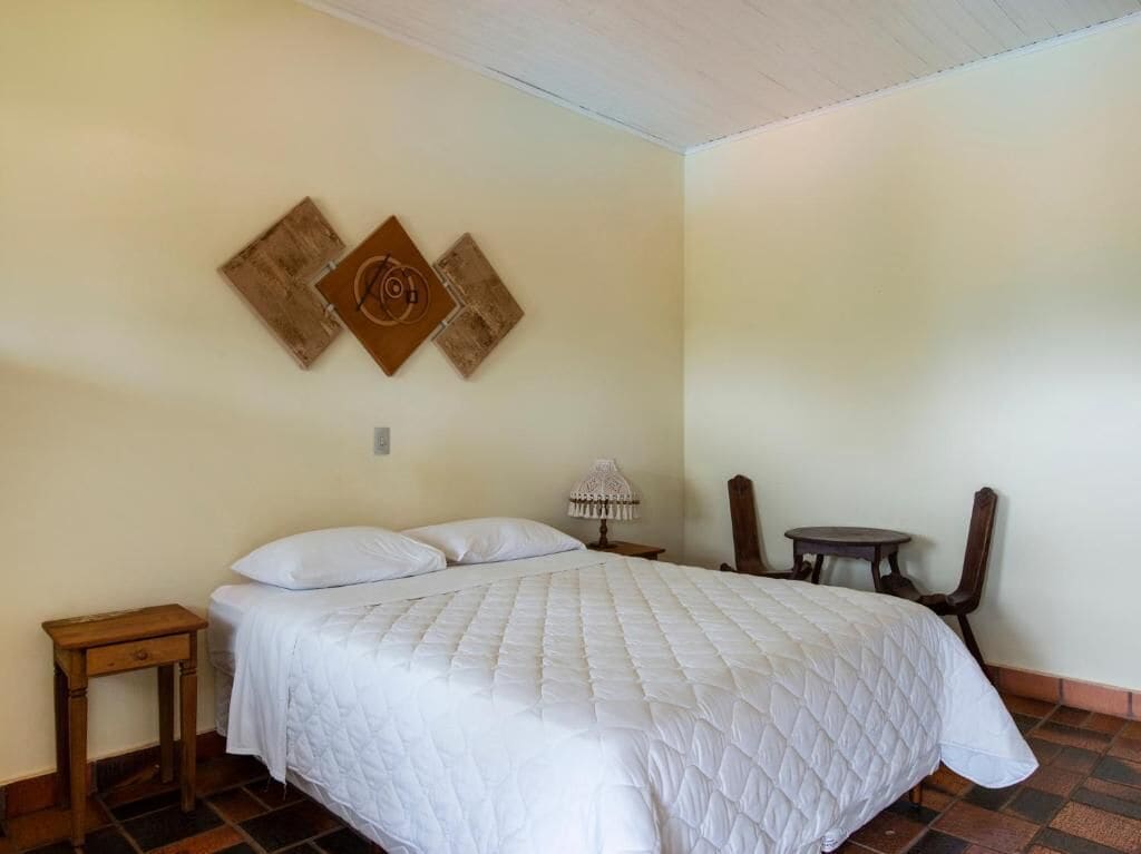 Un dormitorio con cama, mesita de noche, una silla y dos cuadros decorativos.