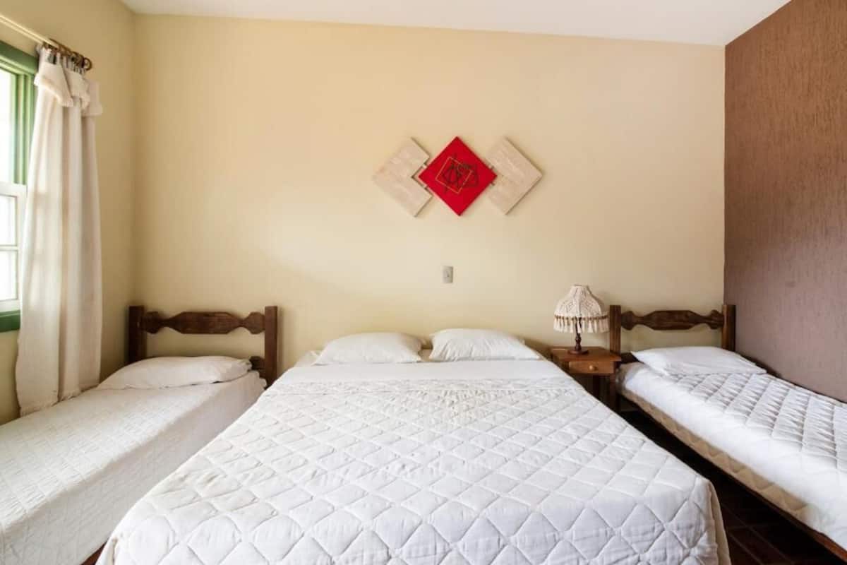 A hotel room with three beds, a wall-mounted red decoration, and a bedside lamp.