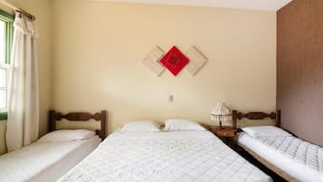 Quarto de hotel com três camas, um adorno vermelho fixado na parede e uma luminária de cabeceira.