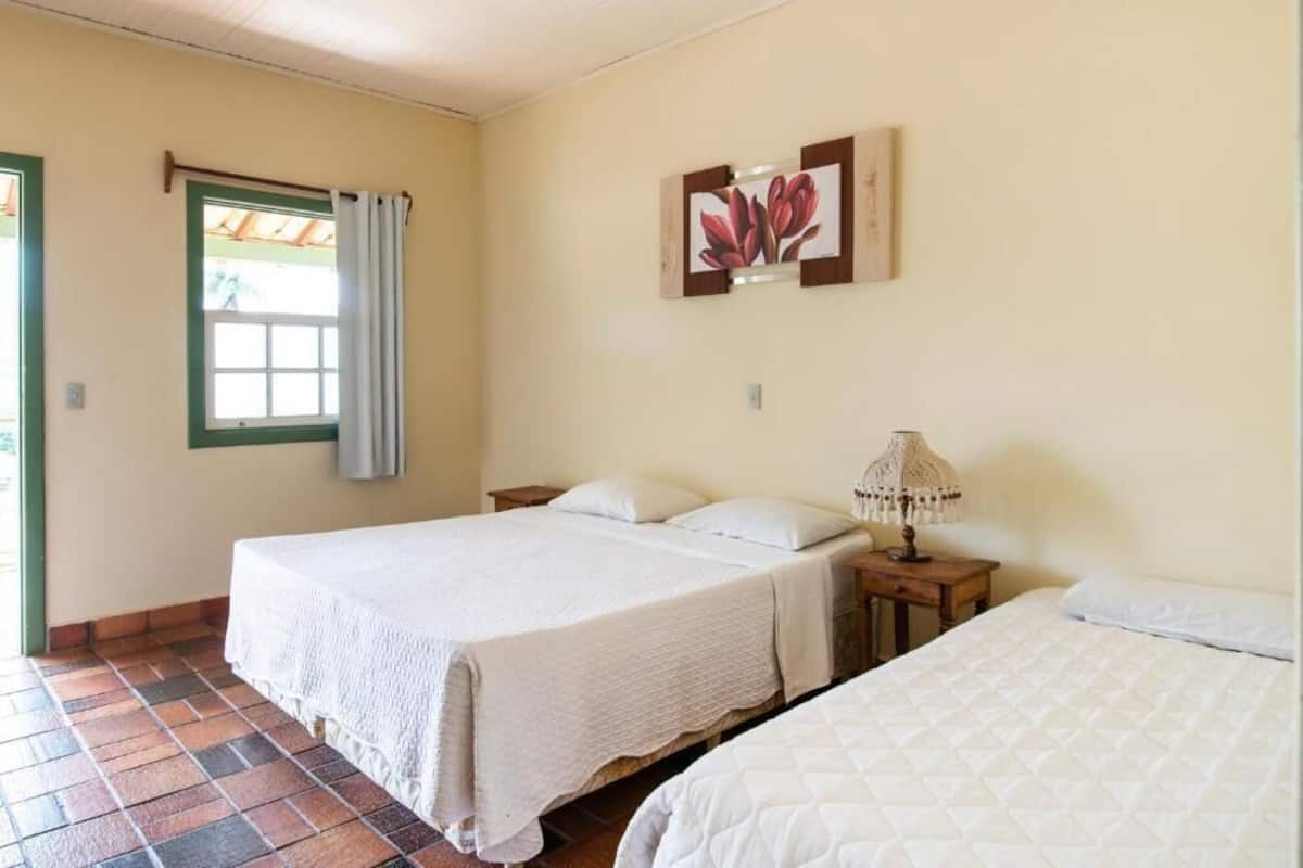 A room with two beds, a window with curtains, a wall-mounted lamp, and a framed picture.