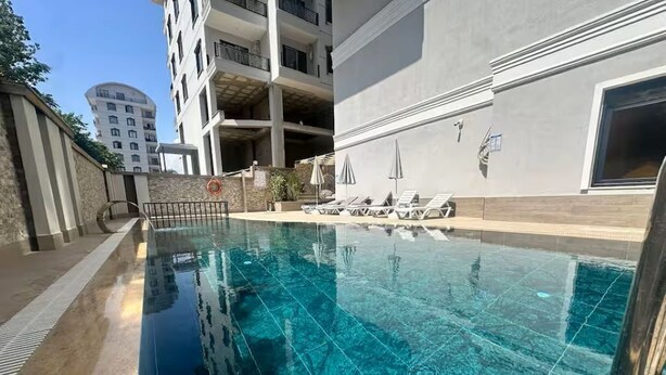 Una piscina con agua cristalina, tumbonas y un edificio con balcones al fondo.