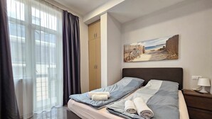 Een slaapkamer met een bed, nachtkastje, schilderij en een raam met gordijnen.