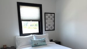 Un dormitorio con una cama, una mesita de noche, una ventana con persianas y un cuadro en la pared.