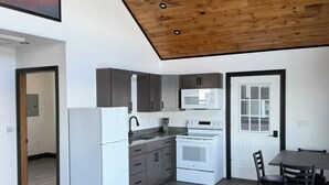 Una cocina moderna con electrodomésticos blancos, un comedor con mesa y sillas, y un techo de madera con iluminación empotrada.
