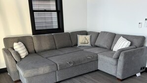 Un sofá seccional gris con piso de madera y una ventana con persianas.