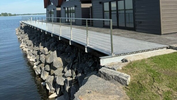 Un edificio frente al agua con una terraza de madera y ventanas amplias.