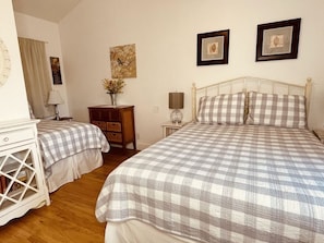 A bedroom with two beds, a nightstand, a dresser, and wall art. - The Garden Cottage at Second Street Cottages (Ashland)