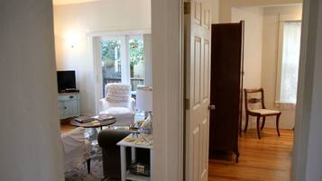 A room with a bed, a small table with items, a chair, a television, and a door leading to another room.