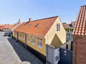 Un bâtiment jaune avec un toit recouvert de tuiles rouges, une petite fenêtre et une porte.