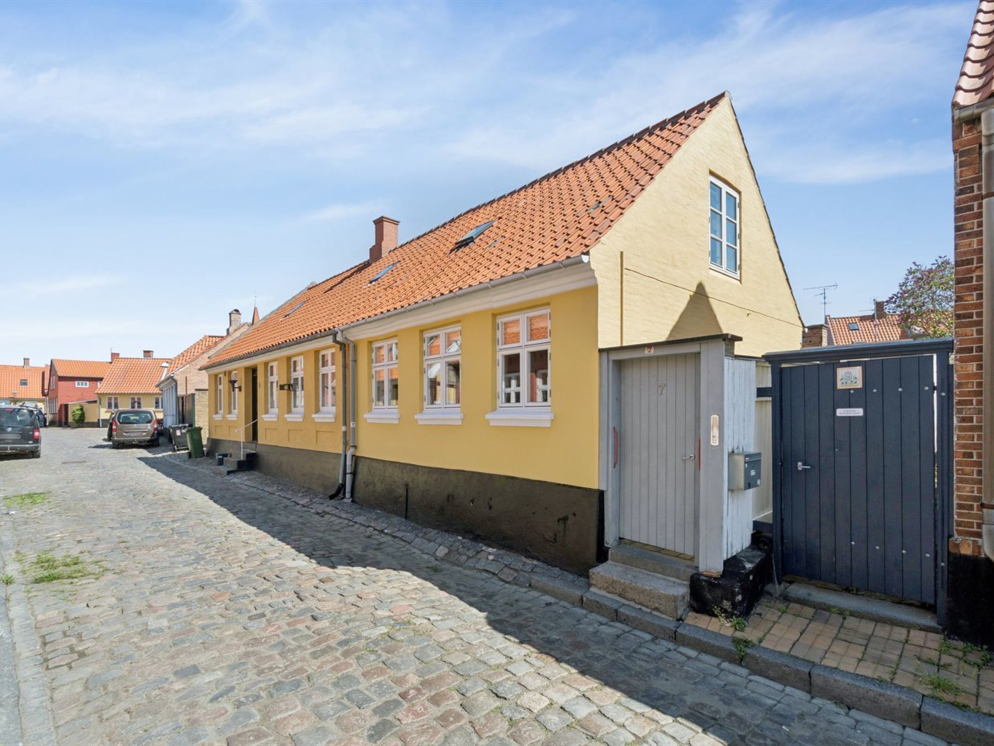 A yellow building with a tiled roof, a garage door, and a cobblestone street.
