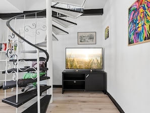Un intérieur moderne agrémenté d’un escalier en colimaçon, d’un téléviseur à écran plat et d’un tableau abstrait aux couleurs vives.