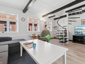 Un salon moderne avec une table blanche, un canapé gris, un escalier en colimaçon et un téléviseur.