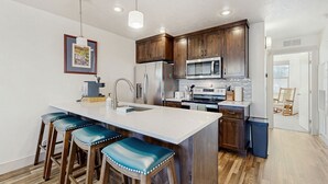 A modern kitchen with a central island, bar stools, stainless steel appliances, and wooden cabinets.
