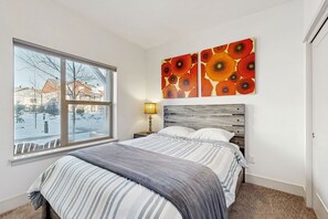 Ein Schlafzimmer mit großem Fenster, einem Bett mit gestreifter Bettwäsche, einem Holz-Kopfschild und einem Wandbild über dem Bett.
