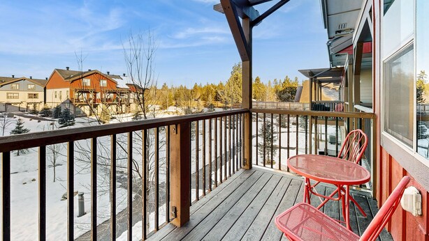 A wooden deck with a railing, two red chairs, and a view of a snowy landscape with buildings in the background.