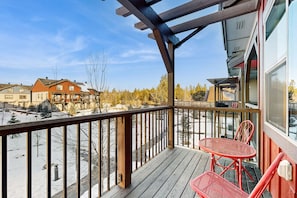 Eine Holzterrasse mit Geländer, zwei rote Stühle und Blick auf eine verschneite Landschaft mit Gebäuden im Hintergrund.