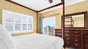 Ein Schlafzimmer mit einem Bett, einem Schminktisch, einem Deckenventilator, einem Fenster mit Jalousien und einem Balkon.