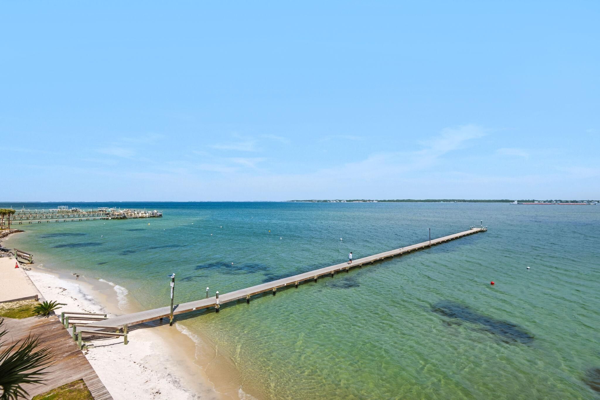 Een steiger die uitsteekt in helder water, met een strand aan één kant.