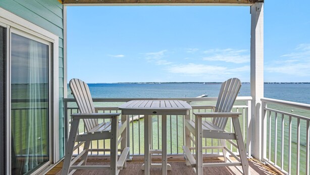 Ein überdachter Außenbereich mit zwei Adirondack-Stühlen und einem kleinen Tisch, mit Blick auf ein Gewässer.