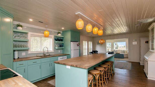 Cocina con armarios color turquesa, encimeras de madera y una isla central con taburetes de bar.