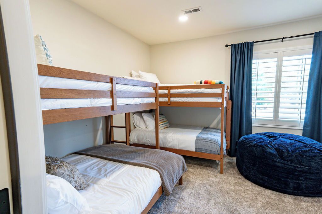 Quarto com beliche, janela, cortinas e um pufe.