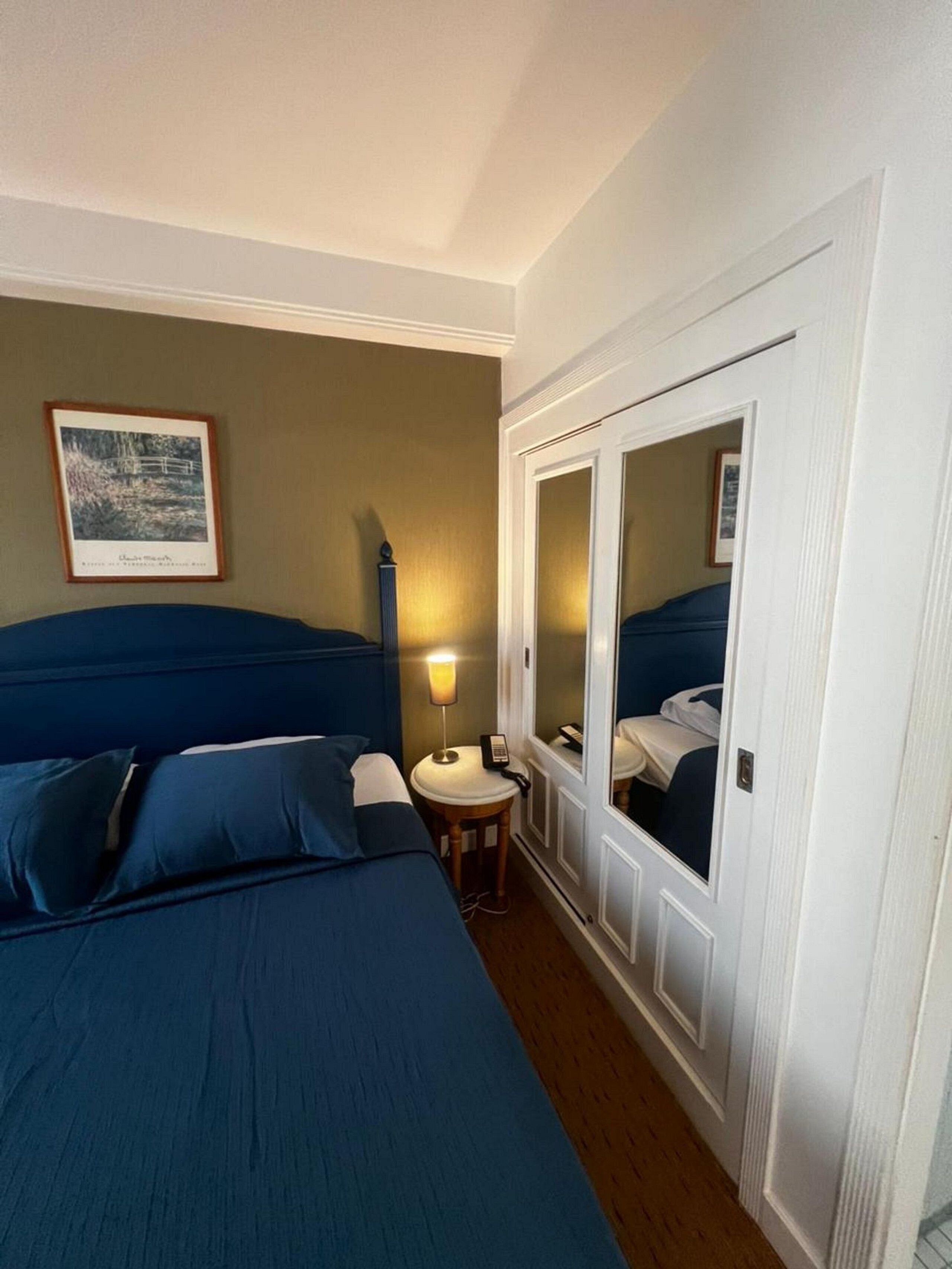 A hotel room with a bed, a bedside lamp, a mirror, and a framed picture on the wall.