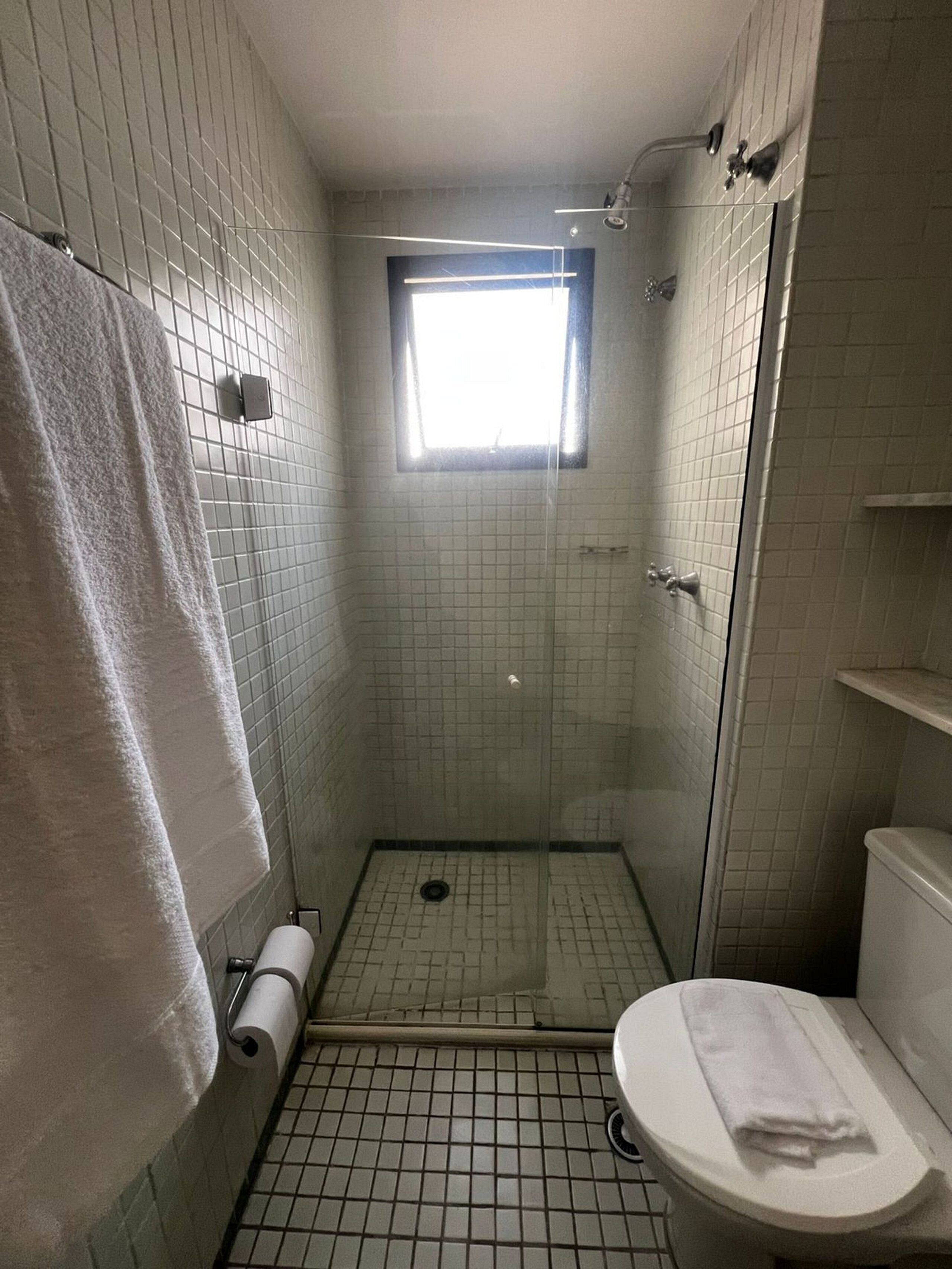 Et lille badeværelse med fliser, en bruser, toilet og et vindue.