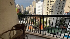A balcony with wicker chairs, a tiled floor, and a view of high-rise buildings and a sports court. - Flat em Moema com Cozinha (São Paulo)