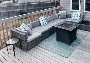 A covered outdoor seating area with a sofa, cushions, and a fire pit.