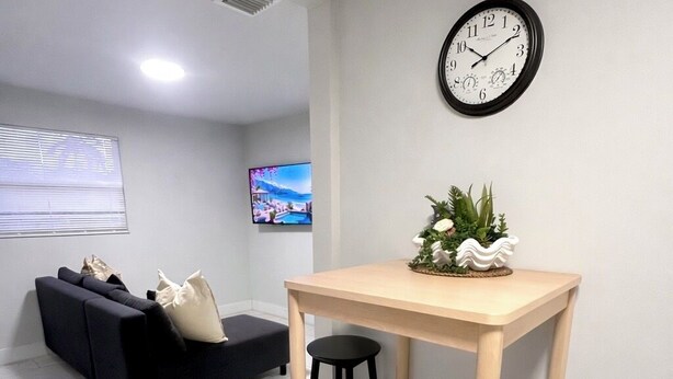 Ett modernt vardagsrum med en soffa, ett matbord med stolar, en väggklocka och en tv.