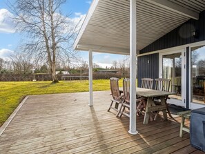 A wooden deck with a table and chairs, a covered area with a white ceiling, and a view of a grassy yard and trees. - "Jytte" - 800m to the fjord by Interhome (Roslev)