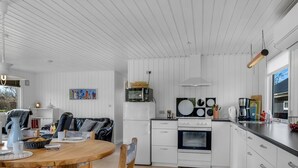 A modern kitchen with white cabinetry, a dining area with a wooden table and chairs, and a view of the outdoors through a window. - "Jytte" - 800m to the fjord by Interhome (Roslev)
