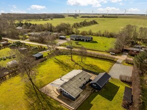 Ein ländliches Anwesen mit einer großen offenen Feldfläche, Windkraftanlagen in der Ferne und einem Bauernhaus mit einer Holzterrasse.