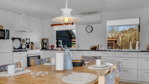 A modern kitchen with white cabinetry, a wooden dining table with placemats, and a hanging light fixture. - "Jytte" - 800m to the fjord by Interhome (Roslev)