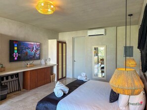 A modern hotel room with a bed, a TV, a desk, and a mirror. - Piece of Paradise: 2BR Apartment with Private Pool in Tulum (Tulum)