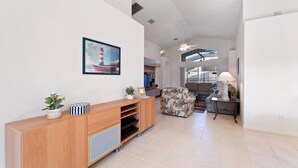 Een ruime woonkamer met een houten entertainmentkast, een gestreept sofa en een eethoek met tafel en stoelen.