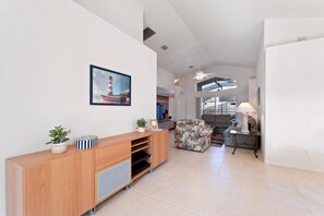 A spacious living area with a wooden entertainment unit, a patterned sofa, and a dining area with a table and chairs. - Elegant Villa with Private Pool in Guard Gated Resort (Davenport)