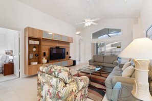 A spacious living area with a flat-screen TV, a sofa, a coffee table, and a ceiling fan. - Elegant Villa with Private Pool in Guard Gated Resort (Davenport)