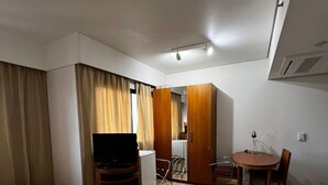 A hotel room with a bed, a desk, a chair, a small table, a television, and a wardrobe. - Elegance Suítes Ibirapuera Moema (São Paulo)