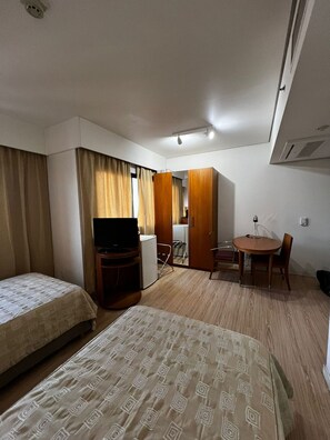 Une chambre d’hôtel équipée d’un lit, d’un bureau, d’une chaise, d’une petite table, d’un téléviseur et d’une armoire.