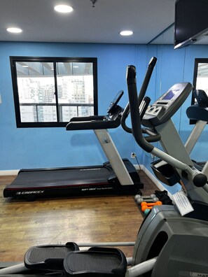 A gym with treadmills, elliptical machines, and a window with a city view. - Elegance Suítes Ibirapuera Moema (São Paulo)