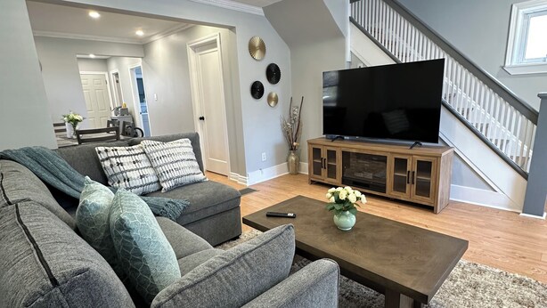 Een moderne woonkamer met een hoekbank, een salontafel, een flatscreen televisie en een trap.