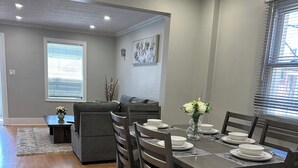 Een eetgedeelte met een houten tafel voor vier personen, omringd door stoelen, en een grijze bank op de achtergrond.