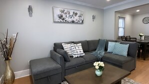 Een woonkamer met een grijze hoekbank, een salontafel en een vloerkleed.