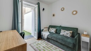 A room with a green sofa, a wooden table, a striped rug, and a sliding glass door. - 2P Studio With Patio Near Paris (Le Pre-Saint-Gervais)