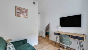 A room with a green sofa, a desk with a chair, a TV, and a small staircase. - 2P Studio With Patio Near Paris (Le Pre-Saint-Gervais)