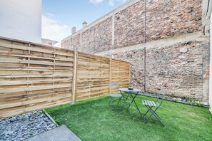 A courtyard with a wooden fence, a brick wall, and a small table with a chair. - 2P Studio With Patio Near Paris (Le Pre-Saint-Gervais)